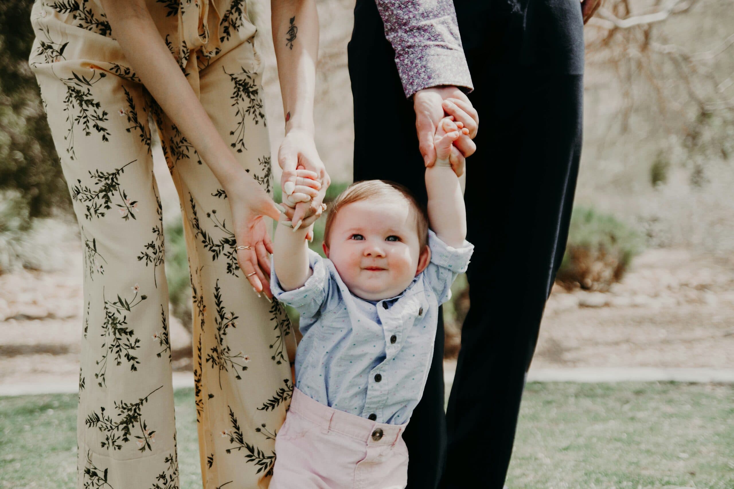 adults assisting a baby to stand
