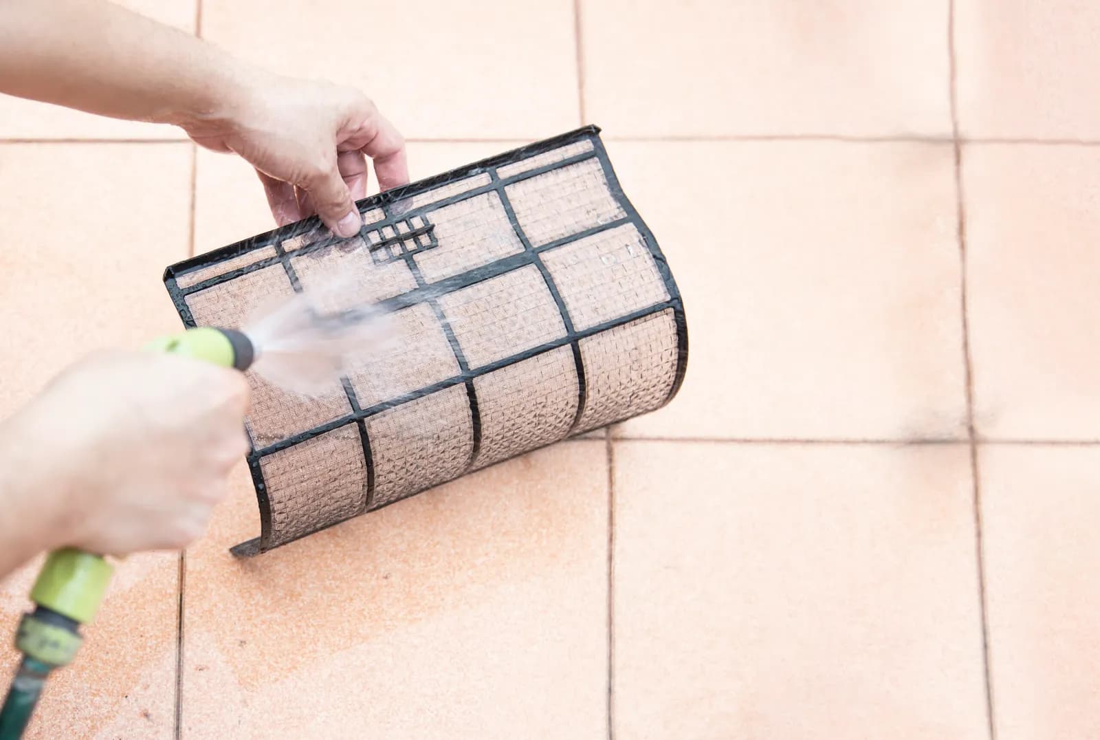 Rinsing a dusty aircon filter with a garden hose